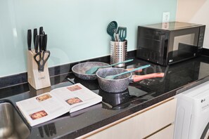 A kitchen with a microwave, a frying pan, a pair of scissors, a knife set, and a recipe book on the counter. - Jalen by Kozystay - Menteng (Central Jakarta)