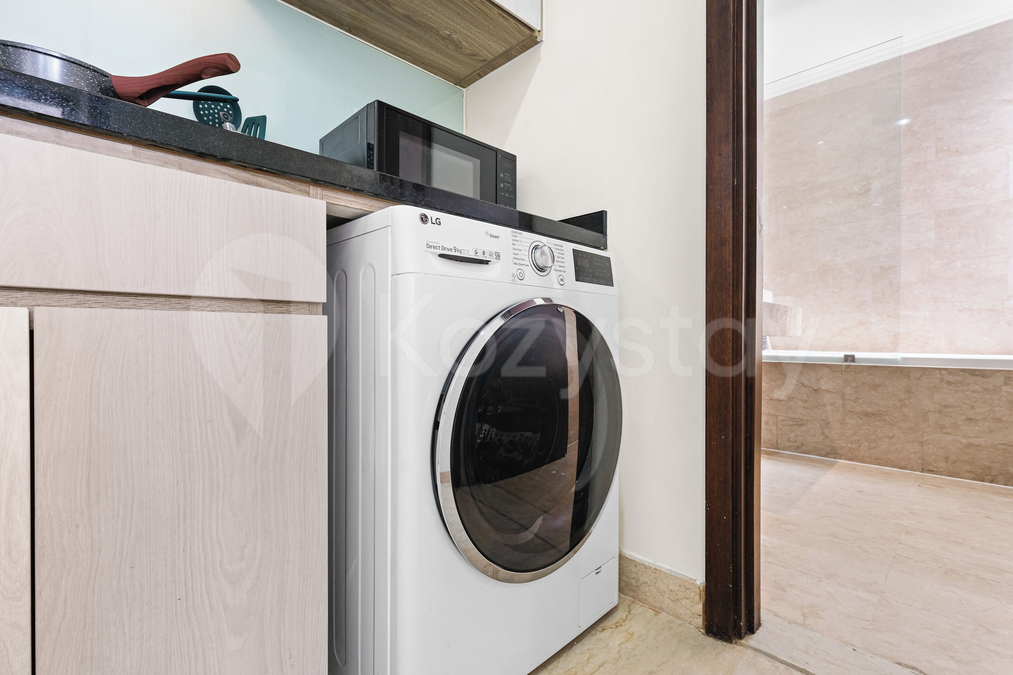 A compact washer and dryer unit in a modern kitchen with light wood cabinetry and a dark countertop.