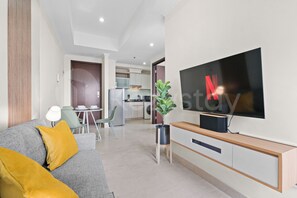 A modern living room with a flat-screen TV, a sofa with cushions, a dining area with chairs, and a kitchen in the background. - Jalen by Kozystay - Menteng (Central Jakarta)