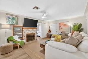 A living room with a fireplace, a television, a guitar, and a couch.