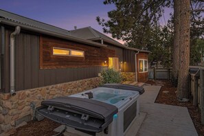 Una cabaña de madera con base de piedra, un jacuzzi y una pequeña terraza.