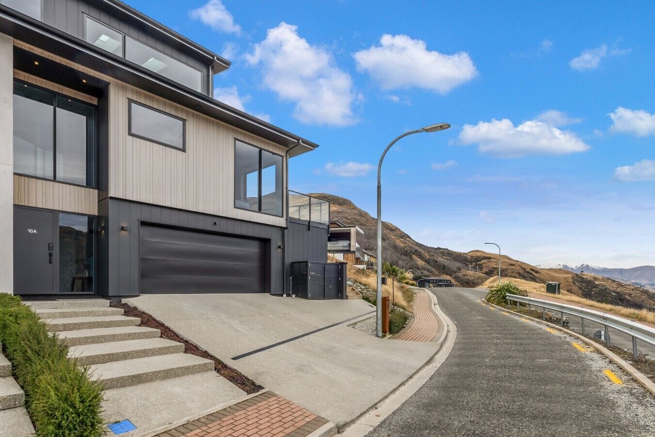 A modern two-story house with a garage, a driveway, and a street with a guardrail.