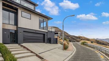 A modern two-story house with a garage, a driveway, and a street with a guardrail.