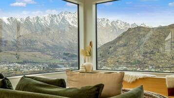 A room with a large window offering a view of snow-capped mountains and a valley below.