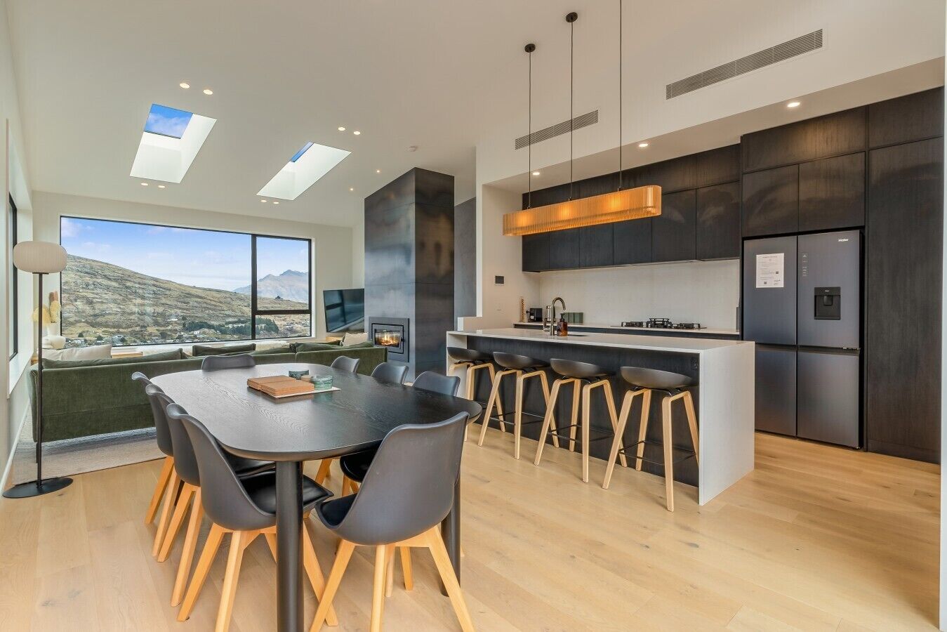 A modern kitchen with a central island, bar stools, and a dining area with a table and chairs.