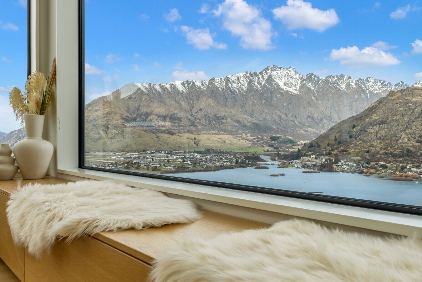 A room with a large window overlooking a mountainous landscape with a lake and a town below.