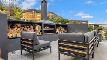 An outdoor seating area with a wood-burning stove, a cylindrical structure, and a view of a hilly landscape.