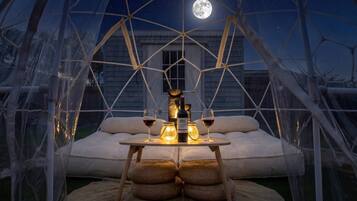 A cozy, geometrically structured outdoor seating area with a table set for two, under a clear night sky with a visible moon.