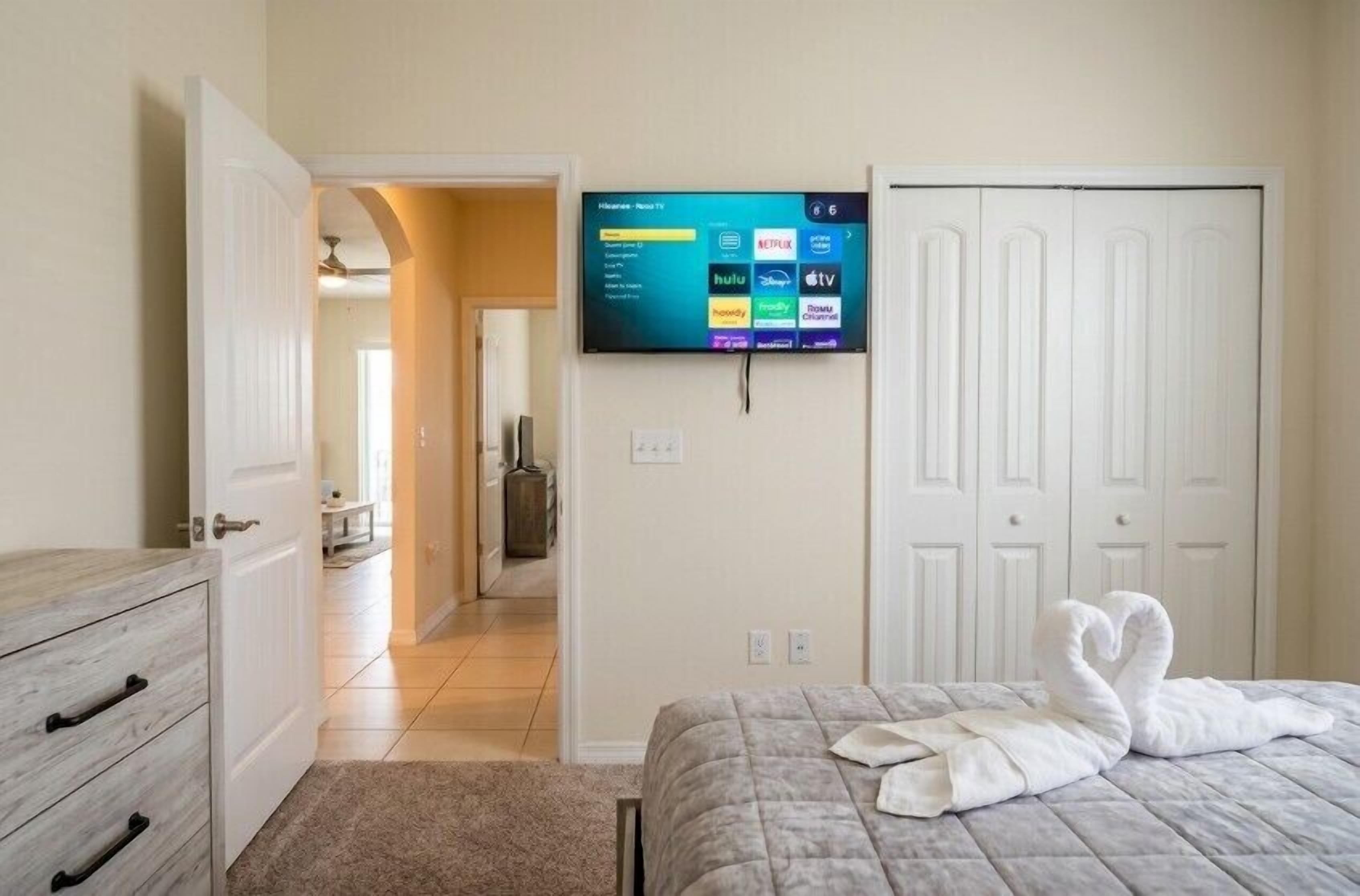Ein Hotelzimmer mit einem Bett, einem an der Wand befestigten Fernseher, einem Schrank und einer Tür zu einem anderen Raum.