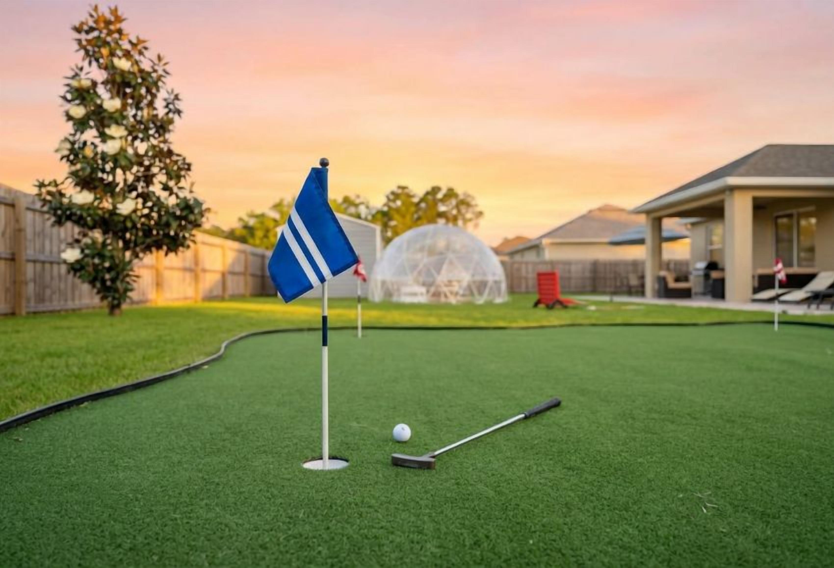 Ein Minigolfplatz mit einer Fahne, einem Golfball und einem Schläger auf dem Grün.