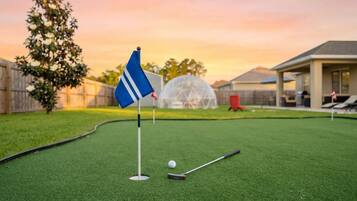 Un campo de mini golf con una bandera, una pelota y un driver en el césped.