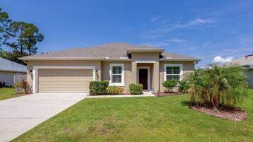 A single-story house with a garage, a front door, and a small front yard with grass and a palm tree.