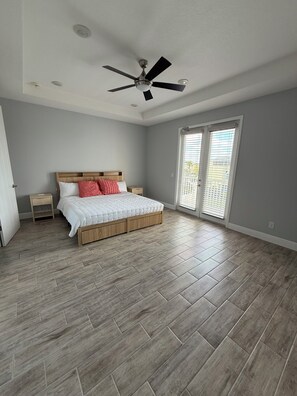 Ein Schlafzimmer mit einem Bett, einem Deckenventilator, einem Fenster mit Jalousien und Holzboden.