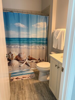 Ein Badezimmer mit Strand-Duschvorhang, Toilette und Holzboden.