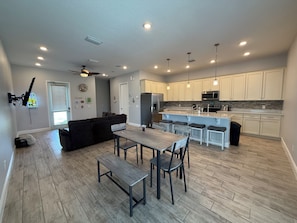 A modern kitchen with white cabinets, a central island, and a dining area with a bench and chairs. - Paradise Cove Spacious 5BR Home with Private Pool in Kissimmee (Kissimmee)