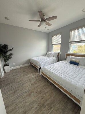 Ein Schlafzimmer mit zwei Betten, einem Deckenventilator und einer Topfpflanze.