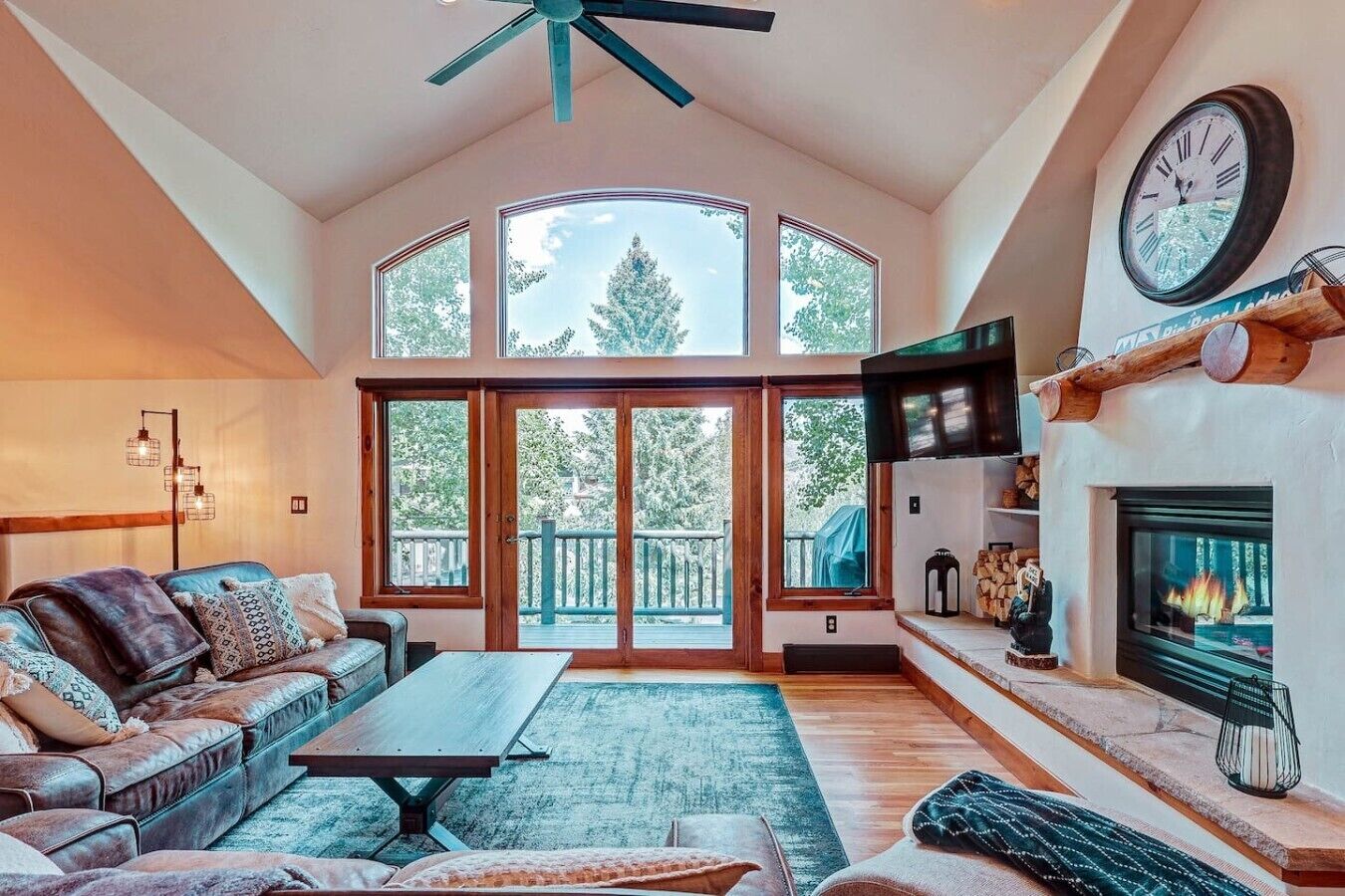 Ein großzügiges Wohnzimmer mit hohen Decken, einem Kamin, einer großen Uhr und Blick ins Freie.