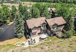 A two-story house with a patio, surrounded by trees and a golf course in the background. - Edwards 4BR, Hot Tub,  Mountain Views & Near Vail (Edwards)