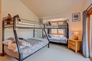 Une chambre avec des lits superposés, une fenêtre avec des rideaux, une table de chevet avec une lampe et un tableau encadré au mur.