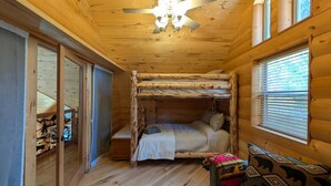 A wooden cabin room with a bunk bed, a ceiling fan, and a window with blinds.