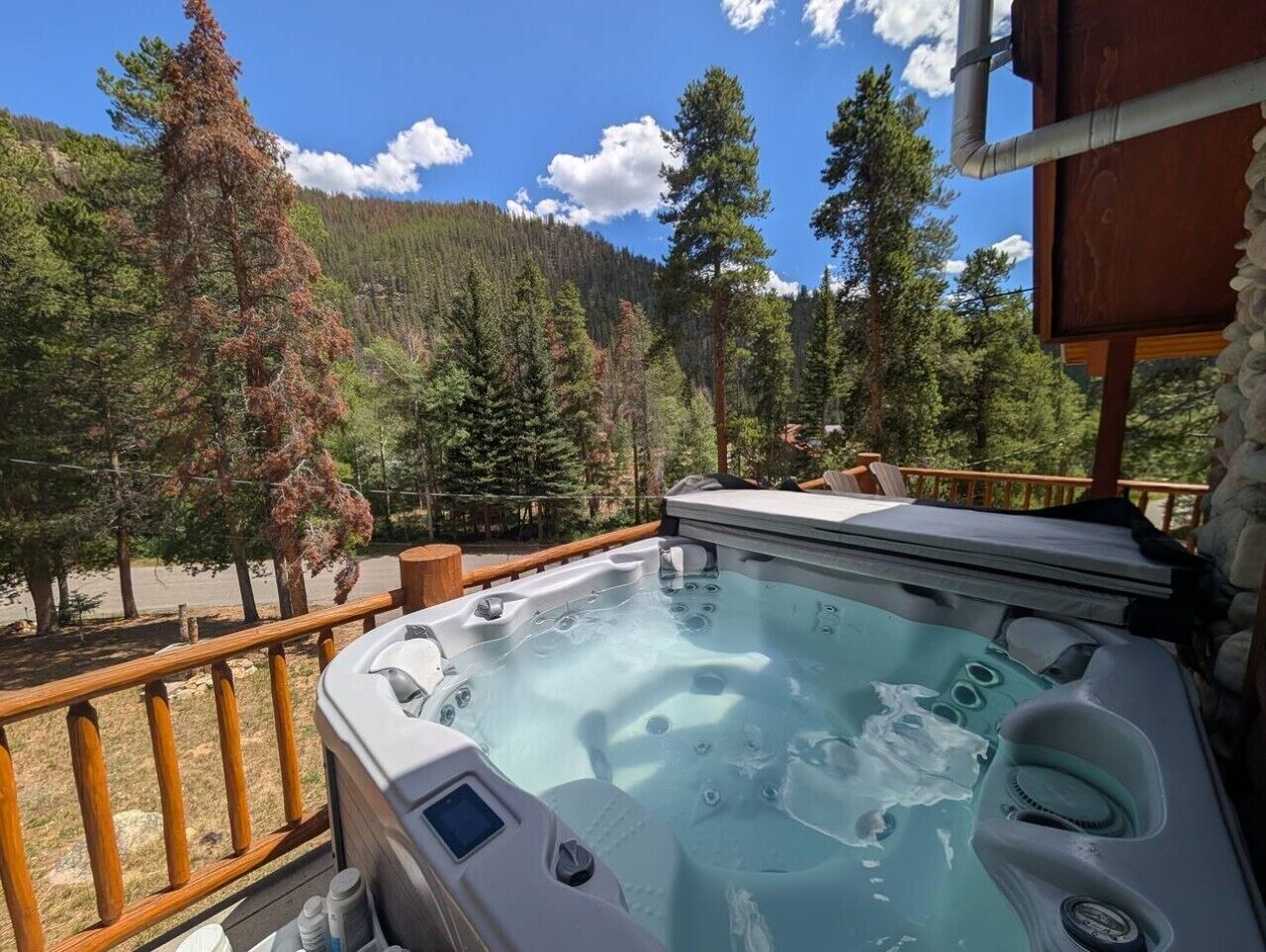 Un bain à remous doté d’un panneau de commande, entouré d’une terrasse en bois et offrant une vue sur une zone boisée.