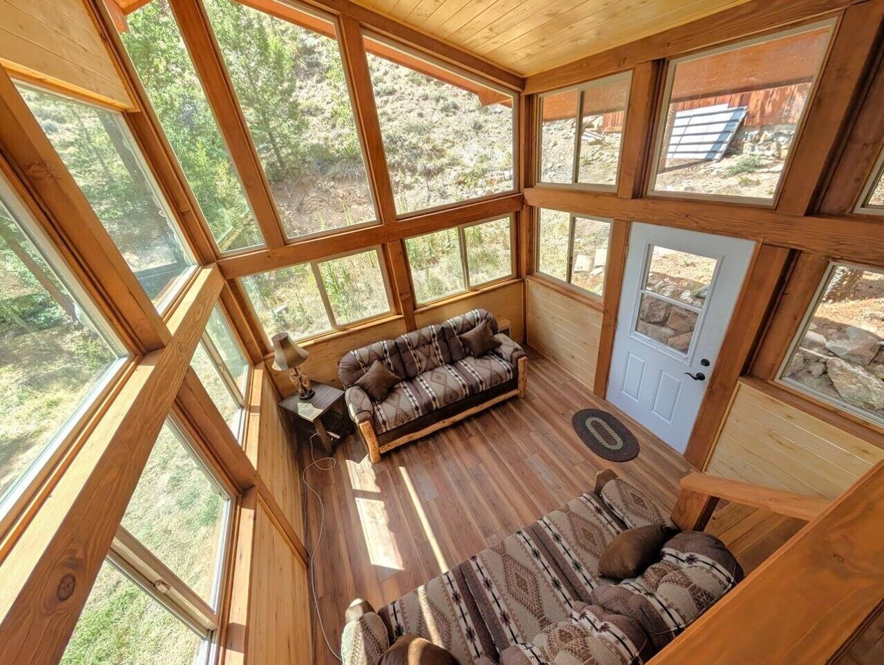 Une pièce avec un plancher en bois, un canapé, une porte et de grandes fenêtres.
