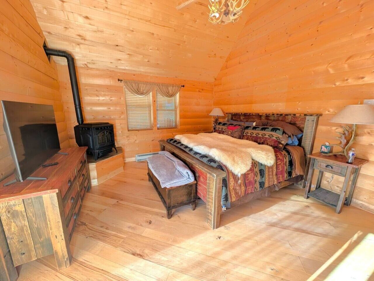 A cozy cabin interior with a bed, a fireplace, a television, and a small table.