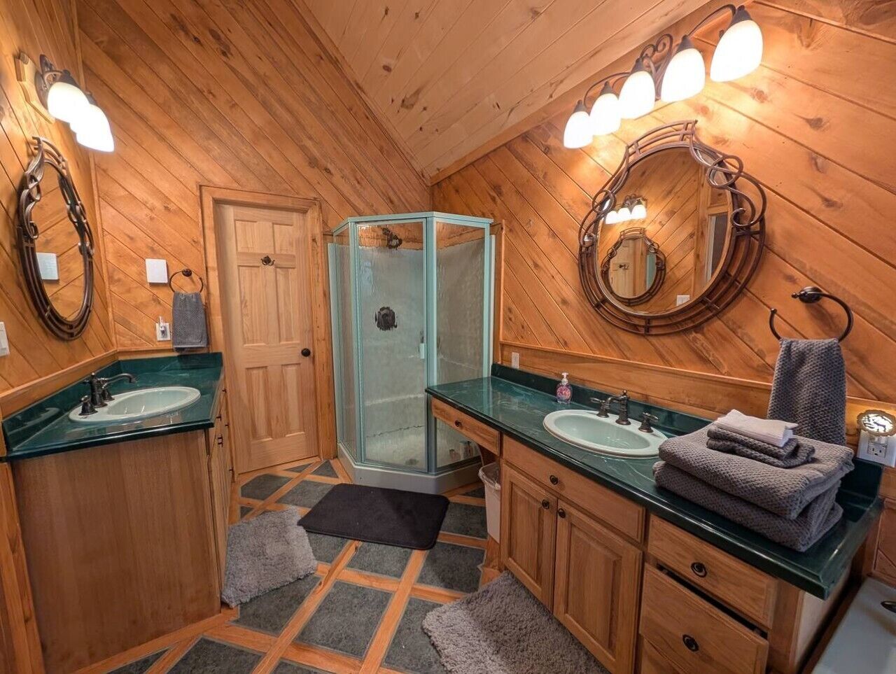 Une salle de bain aux murs lambrissés, dotée de deux lavabos, d’une douche en verre et d’un miroir avec éclairage intégré.
