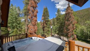 A hot tub on a wooden deck with a view of trees and mountains.