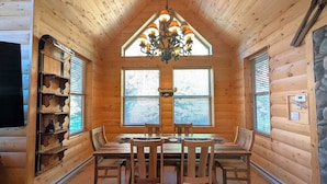 A wooden interior with a dining table, chairs, a chandelier, and a stone accent wall.