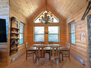 A wooden interior with a dining table, chairs, a chandelier, and a stone accent wall. - Almont Mountain Cabin | Hot Tub & Forest Views (Almont)