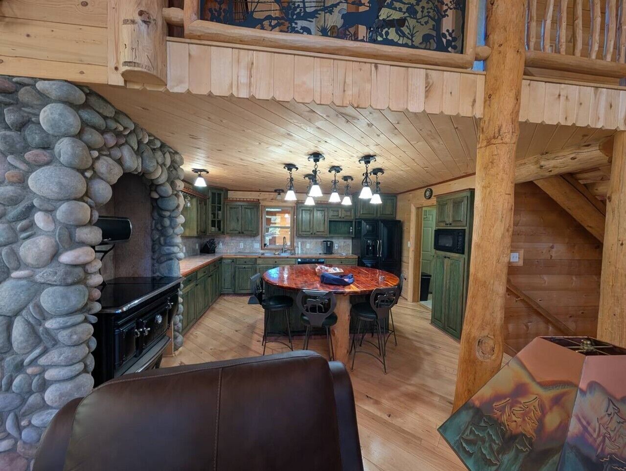 L’intérieur d’un chalet rustique est agrémenté d’une cheminée en pierre, d’un plafond en bois et d’un coin repas avec une table ronde.