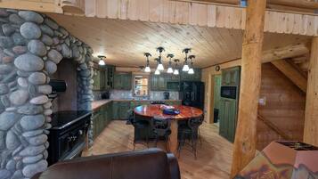 L’intérieur d’un chalet rustique est agrémenté d’une cheminée en pierre, d’un plafond en bois et d’un coin repas avec une table ronde.