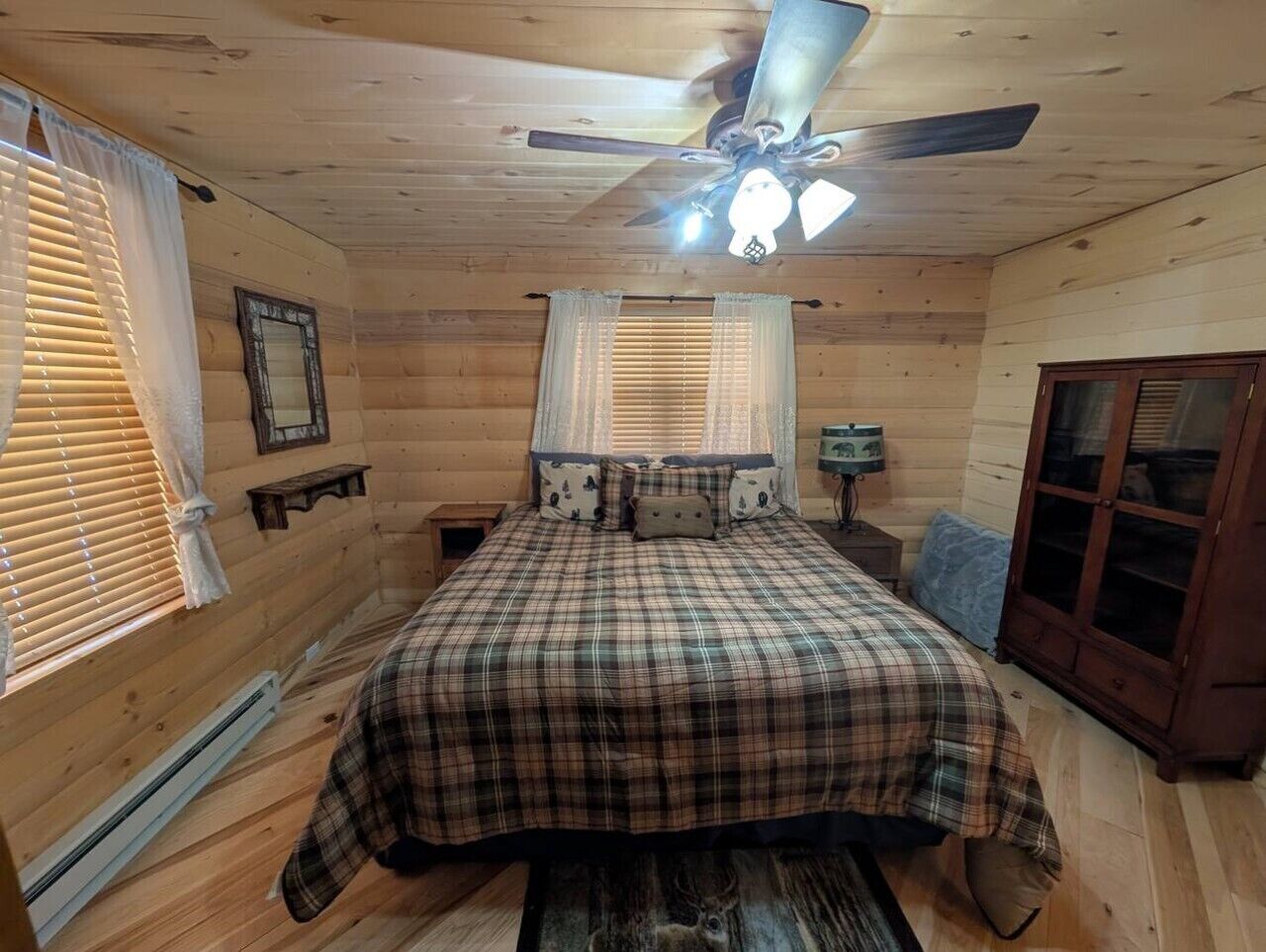 A bedroom with a bed, ceiling fan, window blinds, and a wooden wardrobe.