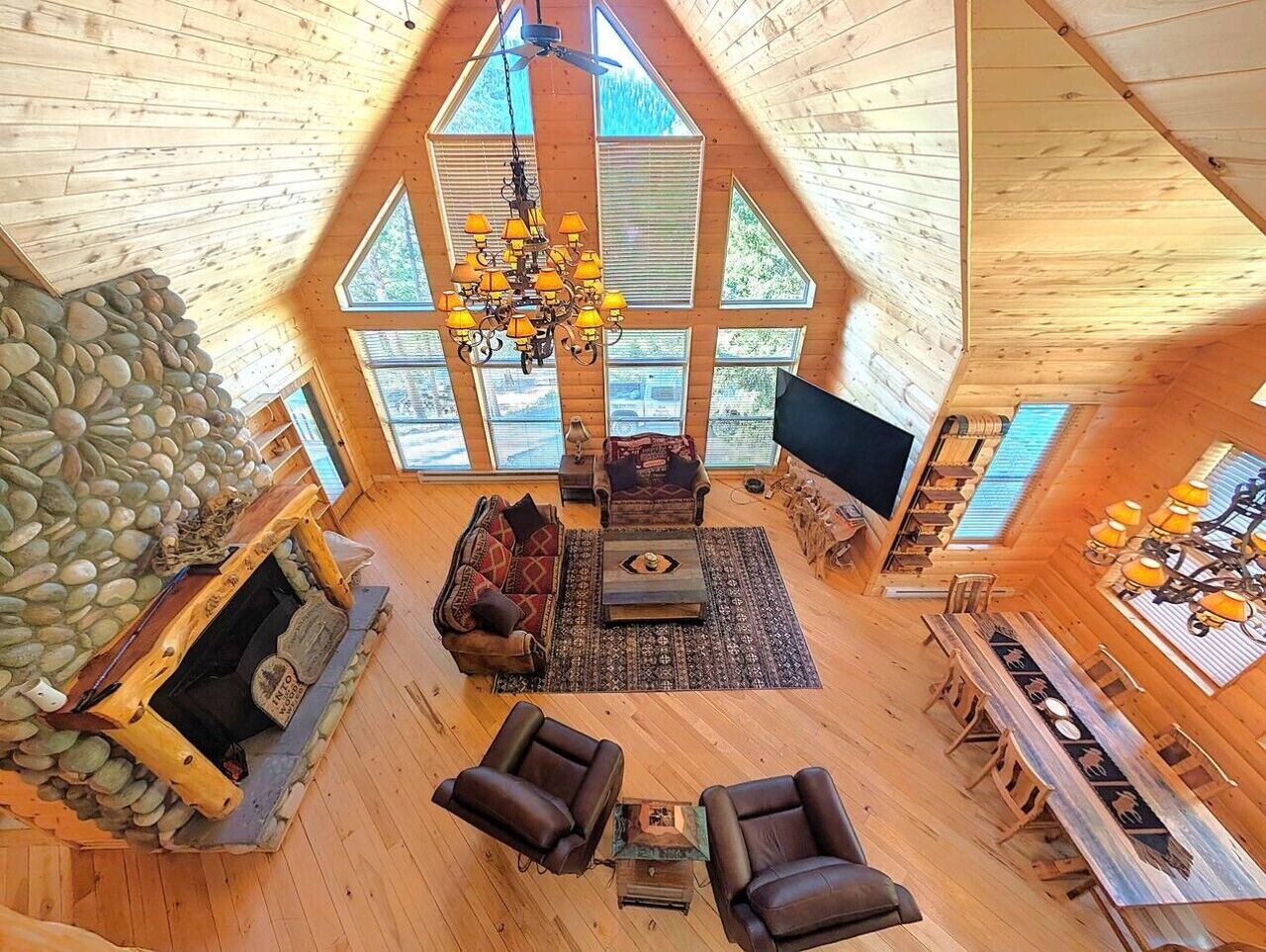 A spacious loft-style living area with a stone fireplace, a large chandelier, and a dining table with chairs.