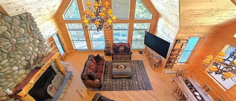 A spacious loft-style living area with a stone fireplace, a large chandelier, and a dining table with chairs.