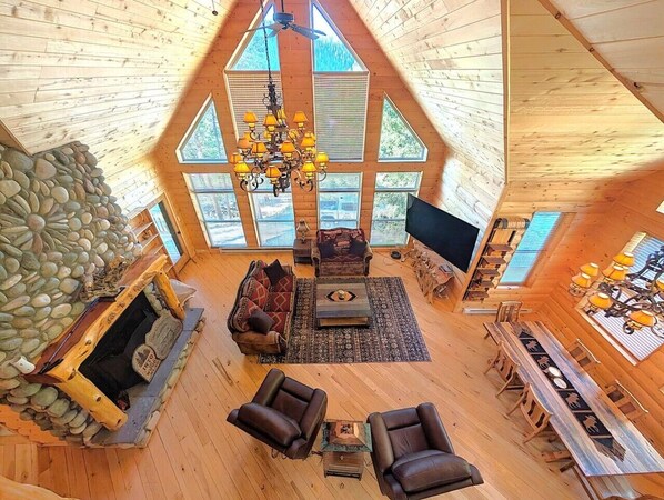 A spacious loft-style living area with a stone fireplace, a large chandelier, and a dining table with chairs.