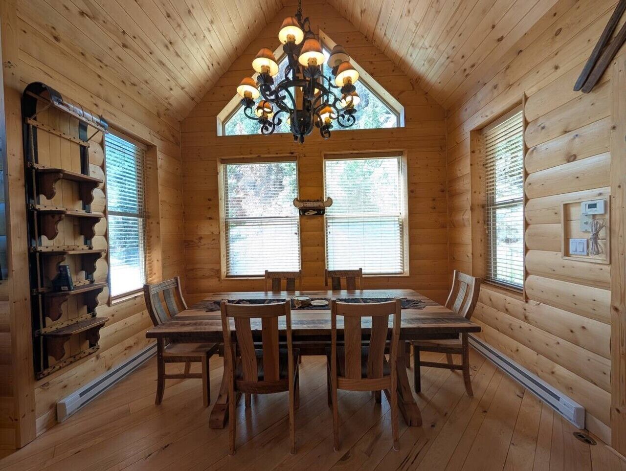 A wooden interior with a dining table and chairs, a chandelier, and built-in shelving.