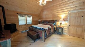 Une chambre dans un chalet en rondins, avec un lit, un radiateur, une fenêtre avec des rideaux, un ventilateur de plafond et une porte.