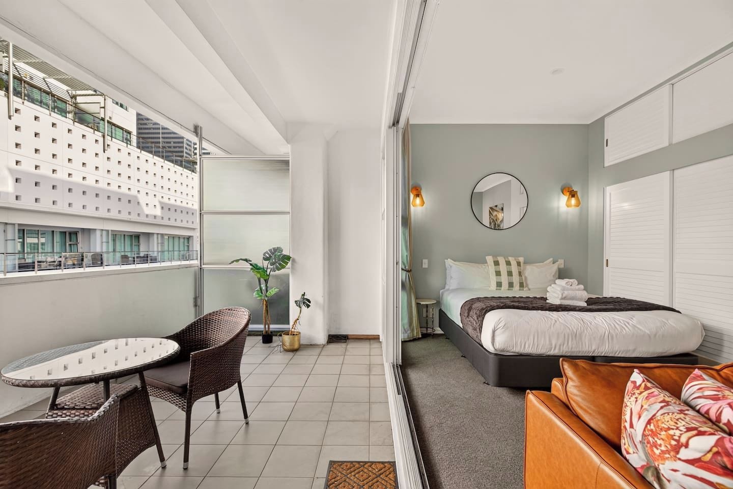 Habitación de hotel moderna con balcón, cama, zona de estar y vista del exterior del edificio.