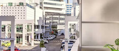 A view of a city street with a modern building, a tower, and parked cars.