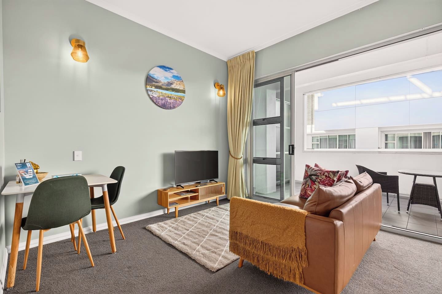 A modern living room with a sofa, TV, and dining area, a large window with curtains, and a painting on the wall.