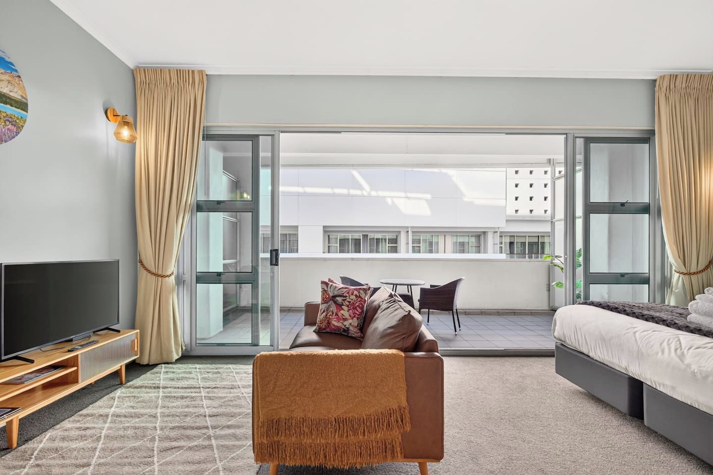 Een moderne hotelkamer met een groot bed, een bank, een televisie en een balkon met uitzicht op de stad.