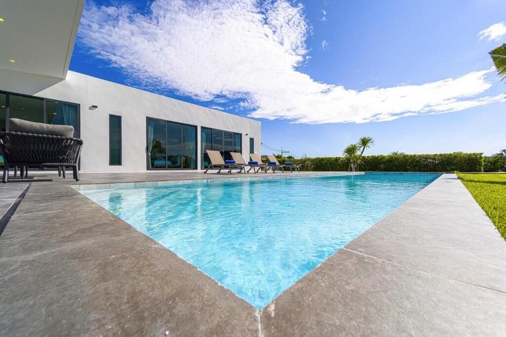A modern building with a swimming pool, lounge chairs, and a clear sky.