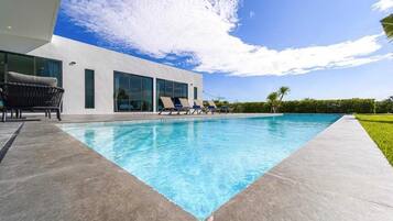A modern building with a swimming pool, lounge chairs, and a clear sky.