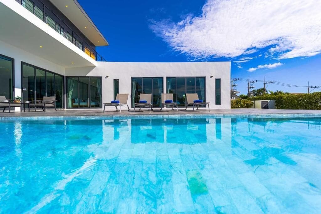 A modern building with a swimming pool, sun loungers, and a clear blue sky.