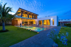 Une maison moderne à deux étages, dotée d’une piscine, de grandes fenêtres et d’une pelouse bien entretenue.