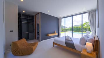 A modern bedroom with a large bed, a built-in wardrobe, a seating area, and a view of a swimming pool.