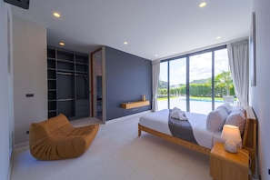 Un dormitorio moderno con una cama grande, un armario empotrado, una zona de estar y vistas a una piscina.