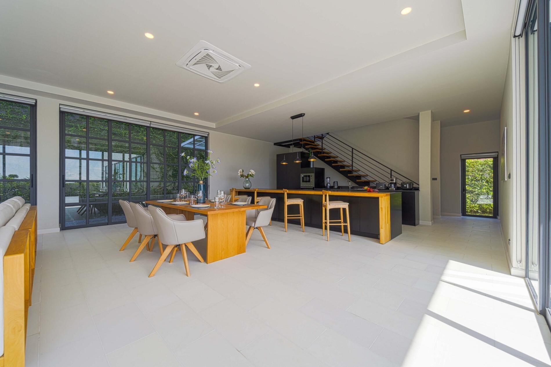 A modern kitchen with a central island, a dining area with a large table and chairs, and a staircase leading to an upper level.